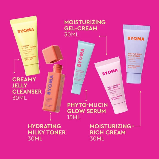 Cinq produits de soin BYOMA disposés sur un fond rose vif avec des étiquettes identifiant chaque article et sa taille.